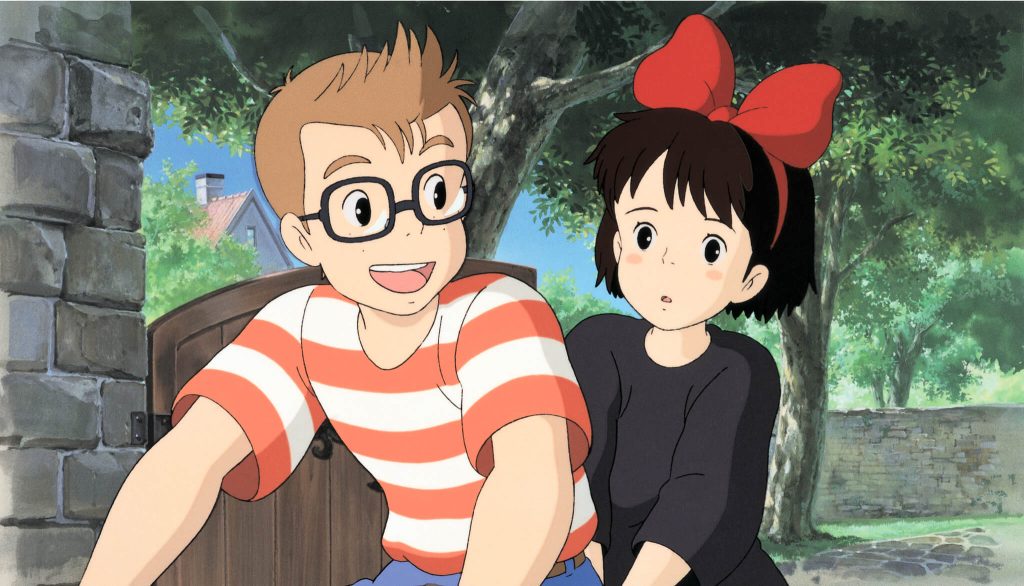 Kiki sitting on a bike with Jiji in a seaside town”